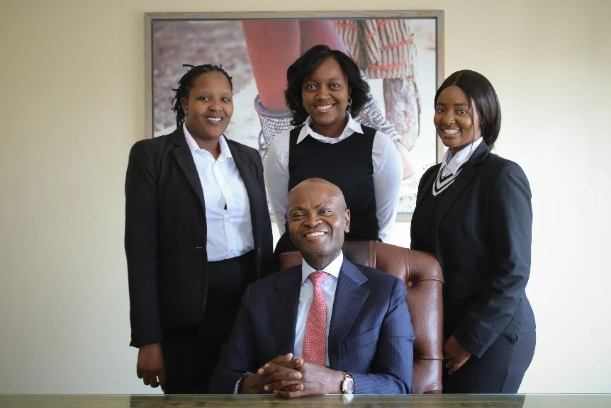 Three team members standing with a seated director in the office